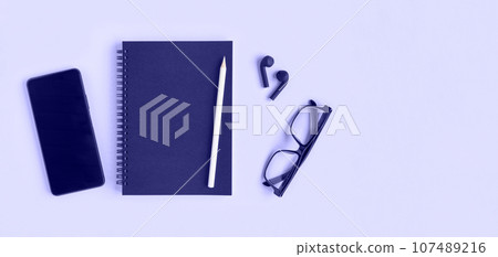 Notebook with pencil, glasses, phone and headphones. Open notebook on purple background, spiral notepad. Top view. Notepad with blank black pages for write, office flat lay. Copy Space, Very Peri Notebook with pencil, glasses, phone and headphones. Open notebook on purple background, spiral notepad. Top view. Notepad with blank black pages for write, office flat lay. Copy Space, Very Peri 107489216