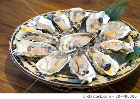 A bounty of fresh oysters resting on crushed ice within a rustic bowl. The bowl is positioned at the center of wooden table. A bounty of fresh oysters resting on crushed ice within a rustic bowl. The bowl is positioned at the center of wooden table. 107490596