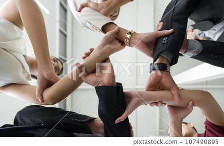 Team building concept. Coworker hold hands and link arms together in a circle, celebrating business success in modern office with high ceiling. Bottom View Team building concept. Coworker hold hands and link arms together in a circle, celebrating business success in modern office with high ceiling. Bottom View 107490895