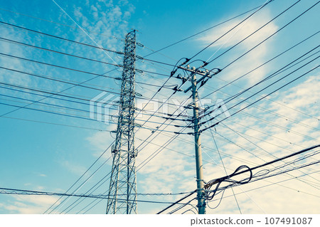 Intersecting high-voltage power lines, electric wires in a residential area, and the autumn sky in warm colors 107491087