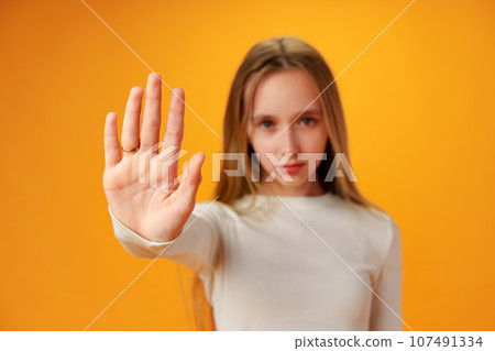Teen girl extend hand in block gesture against yellow background Teen girl extend hand in block gesture against yellow background 107491334