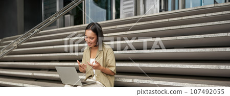 Vertical shot of asian girl student attend online meeting, talking at laptop, video chat, sitting on stairs Vertical shot of asian girl student attend online meeting, talking at laptop, video chat, sitting on stairs 107492055