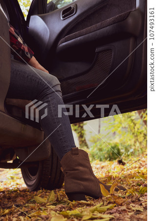 Women's legs in jeans and cowboy boots from an opened car. Women's legs in jeans and cowboy boots from an opened car. 107493161