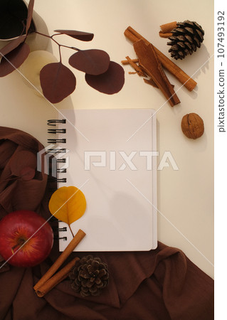 Background for Thanksgiving celebration. A notebook displayed with brown cloth, brown dried leaves, cinnamon stick and nuts on beige background. Creative flat lay for advertising Background for Thanksgiving celebration. A notebook displayed with brown cloth, brown dried leaves, cinnamon stick and nuts on beige background. Creative flat lay for advertising 107493192