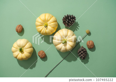 Top view of mini pumpkins decorated with dry pine cones and walnuts on a green background. Unique decoration ideas, warm autumn and happy Thanksgiving 107493222