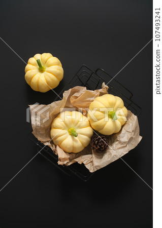 Mysterious black background with mini pumpkins placed on a black plastic basket. Decorative pumpkins for Thanksgiving. Scene for advertising, minimalist concept Mysterious black background with mini pumpkins placed on a black plastic basket. Decorative pumpkins for Thanksgiving. Scene for advertising, minimalist concept 107493241