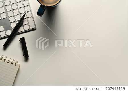 Above view of a coffee cup, notepad, keyboard and mouse on white office desk. Copy space for text 107495119