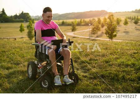 A person with a disability working as a freelancer uses a tablet from a wheelchair at sunset 107495217