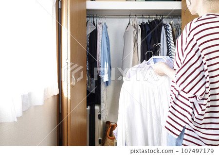 A woman stands with clothes in front of the closet 107497179