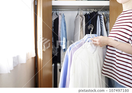 A woman stands with clothes in front of the closet 107497180
