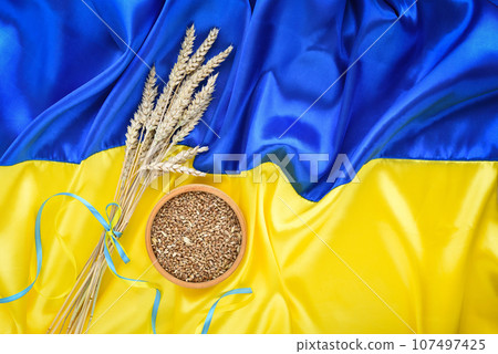 Wheat spikelets and bowl with wheat grains on the background of the flag of Ukraine 107497425