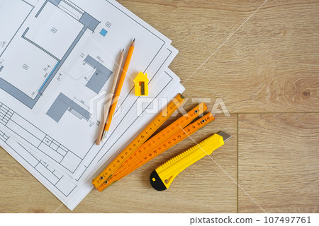 Architectural drawings and pencils, ruler, clerical knife on wooden background. Top view. Architectural drawings and pencils, ruler, clerical knife on wooden background. Top view. 107497761