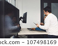 Side view of two colleagues working on a project together developing a new code  107498169