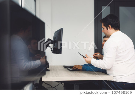Side view of two colleagues working on a project together developing a new code  107498169