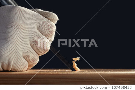 Professional carpenter at work. He is carving wood using a woodworking tools. Glove sleeve with chisel close-up. 107498433