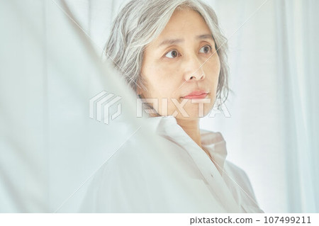 Senior woman standing against white curtain 107499211