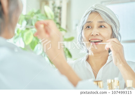 Senior woman applying lipstick Senior woman applying lipstick 107499315