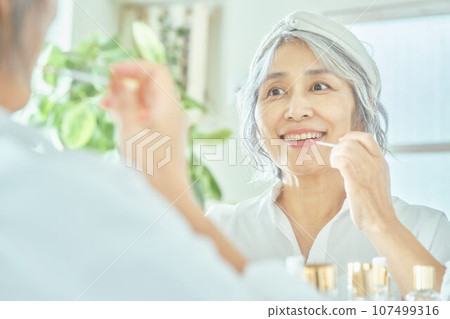 Senior woman applying lipstick Senior woman applying lipstick 107499316