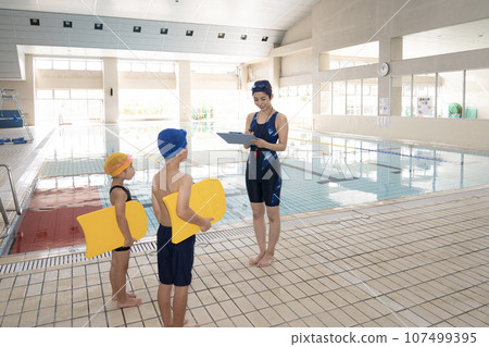 兄弟和游泳班老師在室內泳池裡拿著拍板 107499395