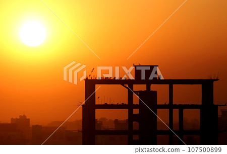 Setting sun behind construction building 107500899