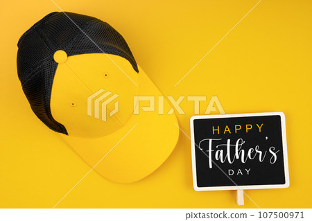 Happy Father's Day on wooden black board and yellow hat on yellow color background. 107500971