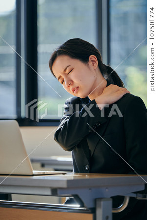 A young woman with stiff shoulders working at a desk 107501774