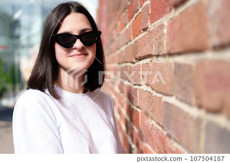 Portrait of a student girl in sunglasses on the background of a city brick wall Portrait of a student girl in sunglasses on the background of a city brick wall 107504187