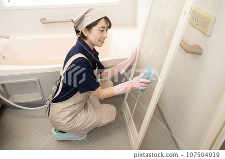 A female house cleaning worker cleaning the bathroom door 107504919