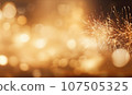 A sparkler emits shimmering light against a golden bokeh background. 107505325