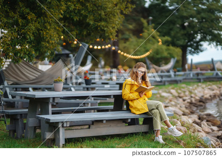 Young woman reading a book in the park. Relaxation, enjoying, solitude with nature. 107507865