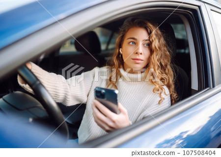Beautiful woman is sitting inside car on drivers seat with phone. Business, taxi, online concert. Beautiful woman is sitting inside car on drivers seat with phone. Business, taxi, online concert. 107508404