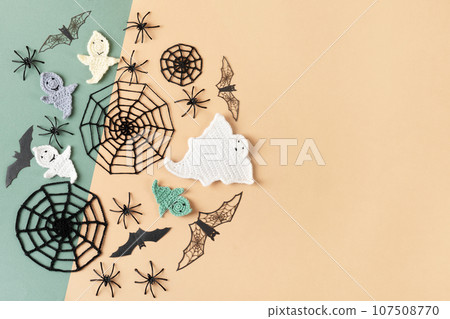 Halloween decorations, ghost, spiders, bats, knitted webs on green and beige background. Halloween greeting card mockup with copy space. Flat lay, top view Halloween decorations, ghost, spiders, bats, knitted webs on green and beige background. Halloween greeting card mockup with copy space. Flat lay, top view 107508770