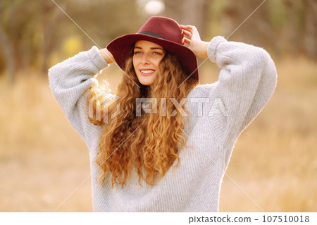Stylish woman in sweater and hat enjoys autumn nature. People, freedom, lifestyle, travel concept. Stylish woman in sweater and hat enjoys autumn nature. People, freedom, lifestyle, travel concept. 107510018
