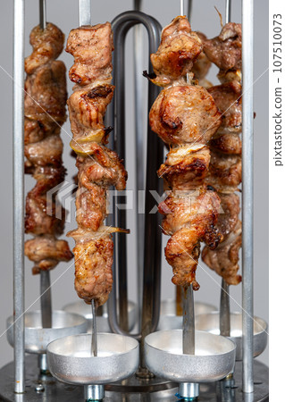 Cooking pork meat in an electric kebab maker on vertical skewers Cooking pork meat in an electric kebab maker on vertical skewers 107510073