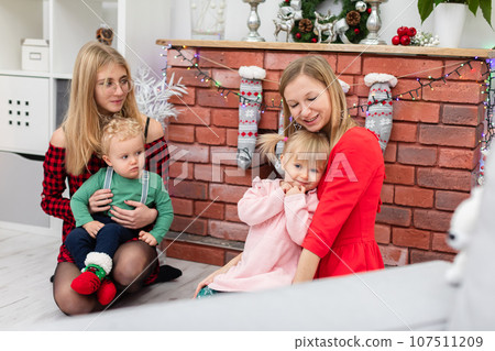 Two women and two children sit by a brick fireplace during the holiday season 107511209