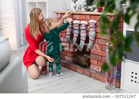 Mom and her little girl spend Christmas time by the fireplace Mom and her little girl spend Christmas time by the fireplace 107511247