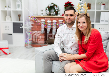 A couple in elegant holiday outfits sits on a gray couch 107511289