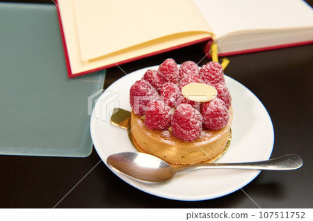 A French tartlet with raspberries and custard near open book on the table 107511752
