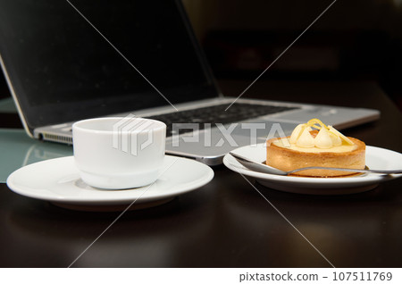 Still life with food and electronical device. A sweet delicious tartlet, cup of coffee over laptop background. Still life with food and electronical device. A sweet delicious tartlet, cup of coffee over laptop background. 107511769