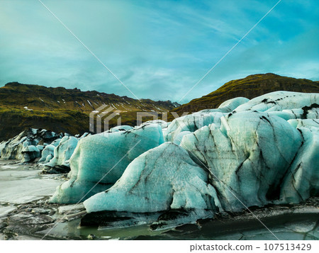 Beautiful ice chunks with blue and green tones appear in majestic Vatnajokull glacier mass, freezing cold waters of Icelandic coast. Drone shot of beautiful route with icebergs and icy high cliffs. 107513429