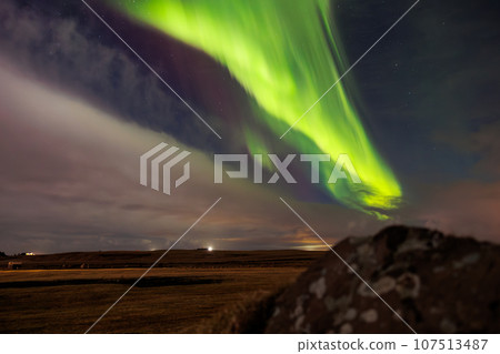 At sundown in Iceland, aurora borealis brightens up night sky in outstanding hues of green and violet, forming magical icelandic landscape. Stars sparkle around northern lights. 107513487