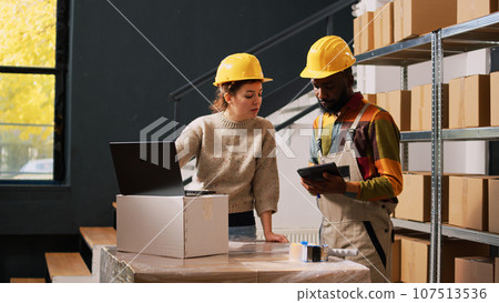 Employees checking cargo stock in depot, examining products inventory list on computer before delivery. Supervisors team working on quality control department, goods production. 107513536