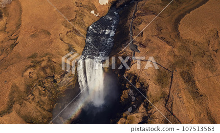 Aerial view of huge cascade in iceland, river flow running down from natural frozen hills. Beautiful nordic skgafoss waterfall flowing off cliffs forming amazing icelandic scenery. Slow motion. 107513563