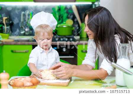 happy family mother and little son preparing dough in kitchen at table. products for dough are on table 107515713