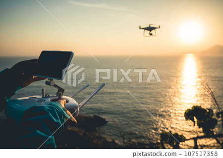 Silhouette of remote control a flying drone which taking photo over sunrise sea 107517358