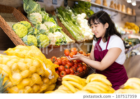 Asian female employee lays out ripe tomatoes on counter and display case Asian female employee lays out ripe tomatoes on counter and display case 107517359