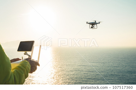Silhouette of remote control a flying drone which taking photo over sunrise sea 107517360