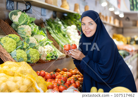 Woman in a veil buys ripe tomatoes in supermarket 107517462