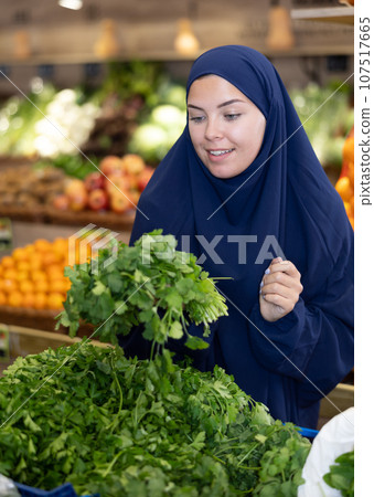 Girl in veil carefully chooses fresh parsley in supermarket 107517665