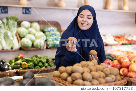 Asian girl in paranja choosing kiwi in grocery 107517738
